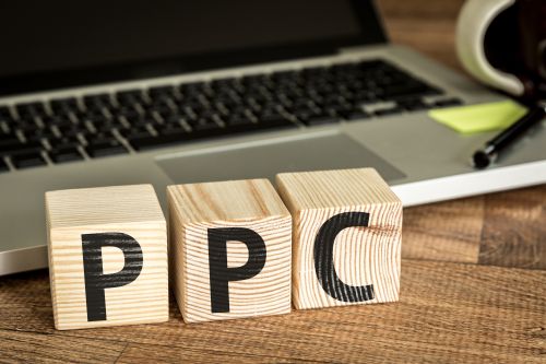 PPC (Pay Per Click) written on a wooden cube in front of a laptop